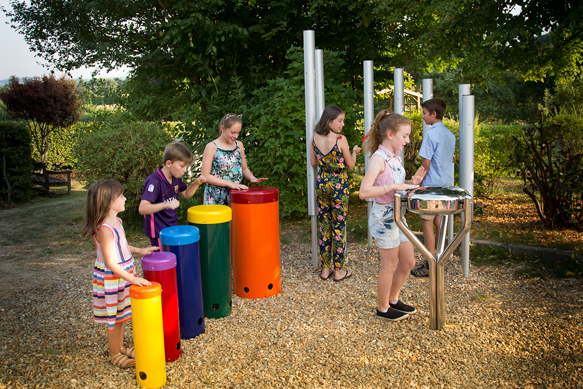 group of six children playing on an ensemble of outdoor musical instruments in a park