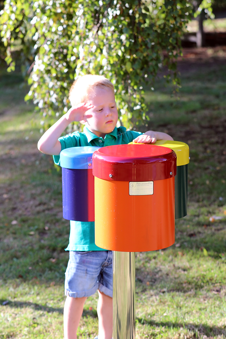 a young boy playing on a set of three colourful outdoor drums in a playground