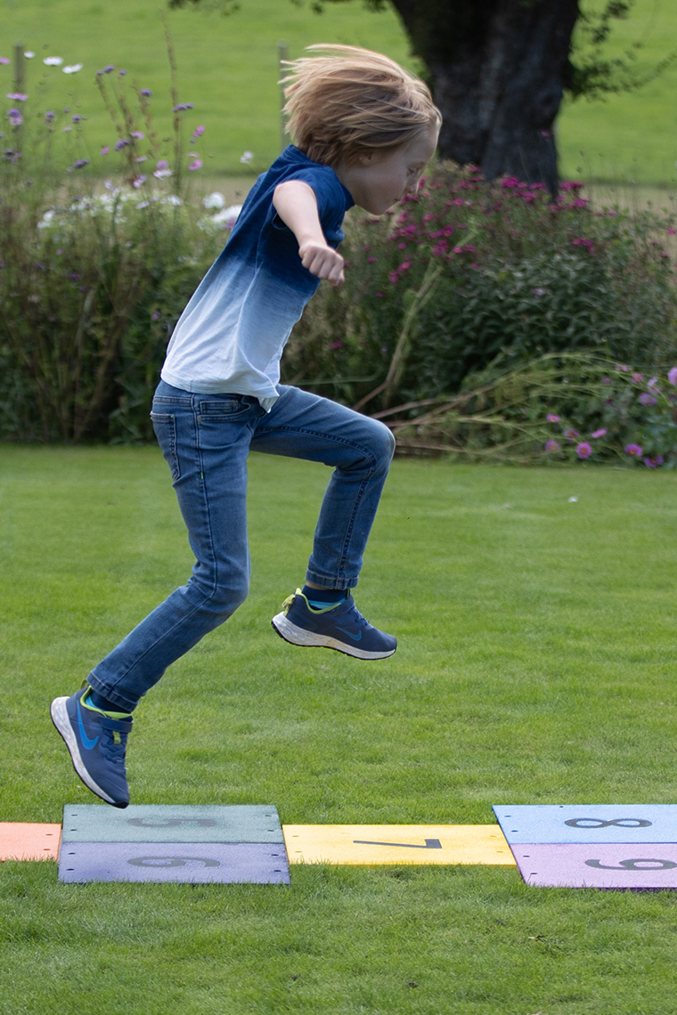 a boy running across a colorful outdoor musical hopscotch installed into grass