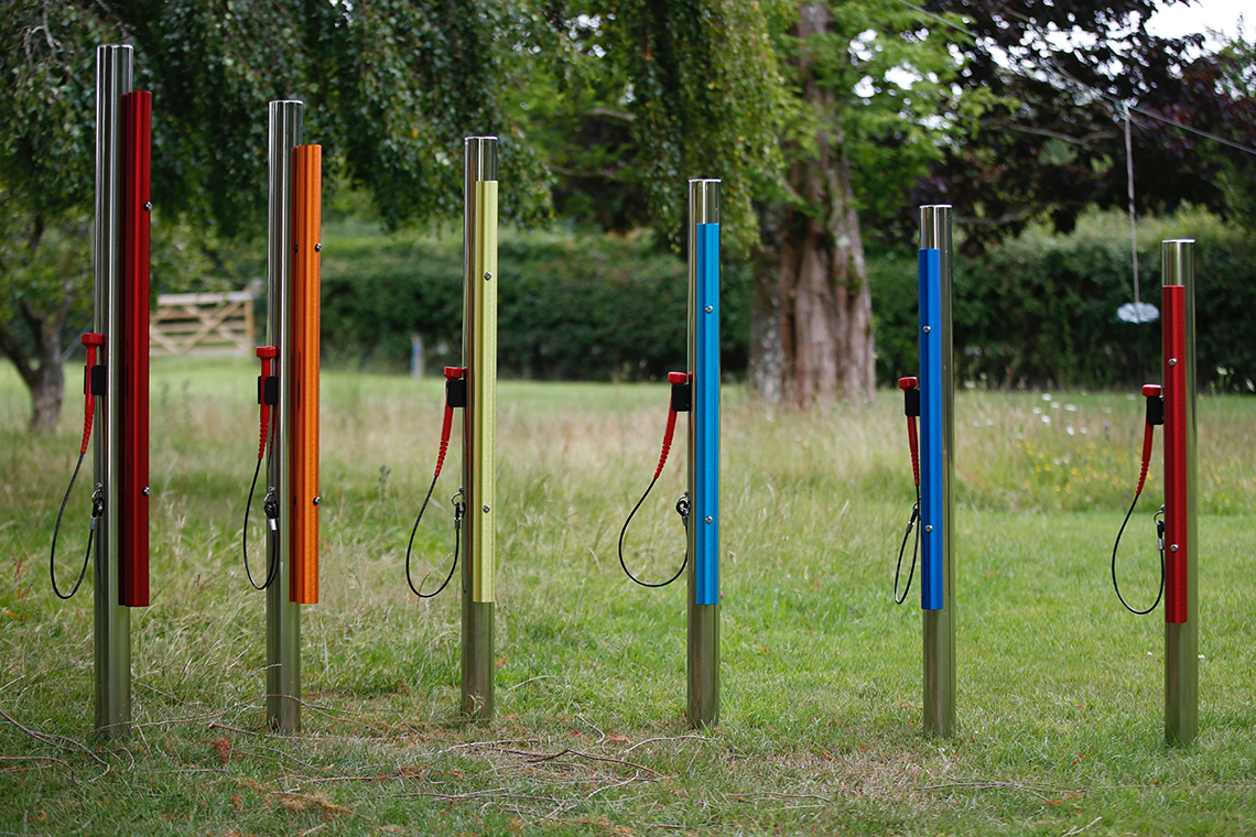 a set of six rainbow colored outdoor musical chimes on stainless steel posts with mallets