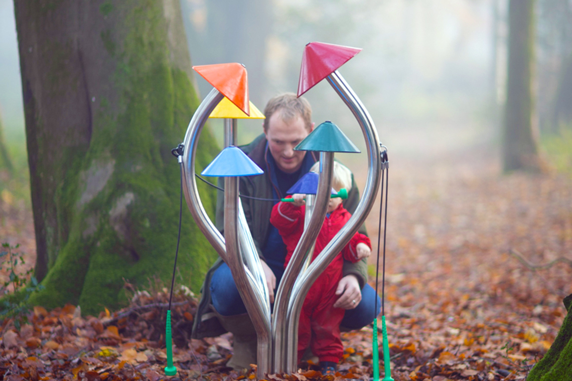 father and son playing colourful outdoor musical chimes shaped like a cluster of mushrooms