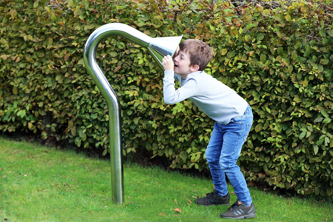 boy speaking into a large stainless steel cone playground talk tube