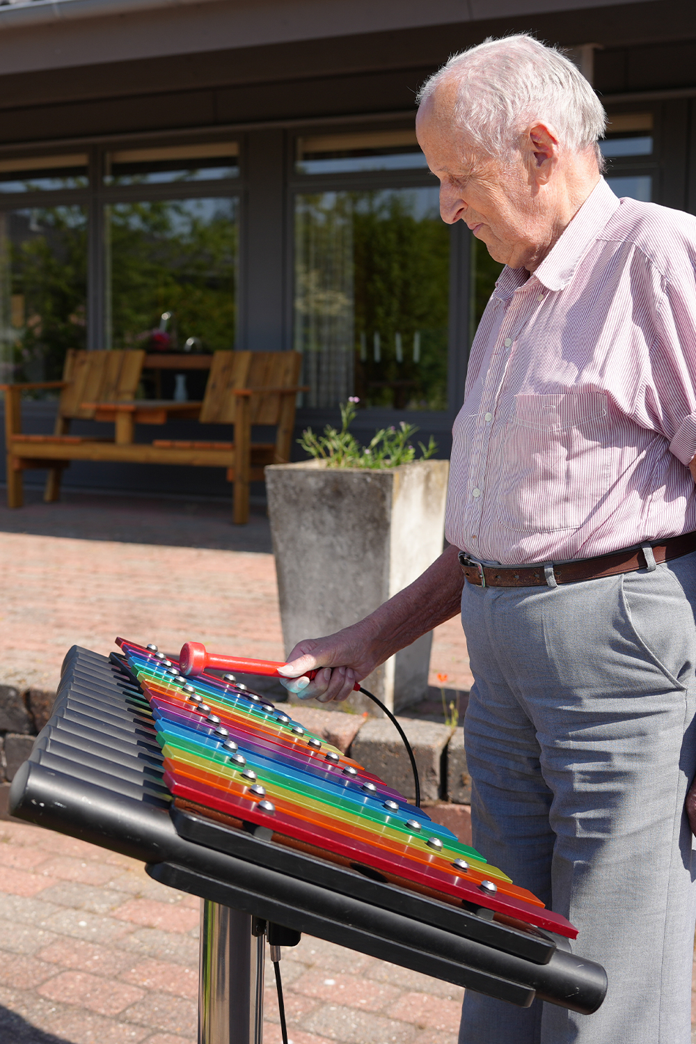 senior male playing a rainbow coloured outdoor xylophone in a care home garden