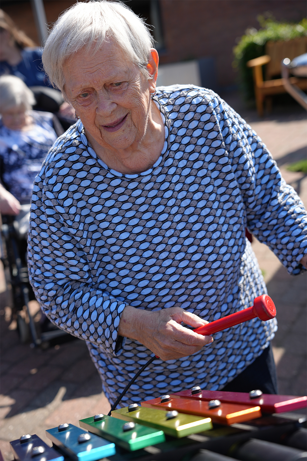 senior lady playing a rainbow coloured outdoor xylophone in a care home garden