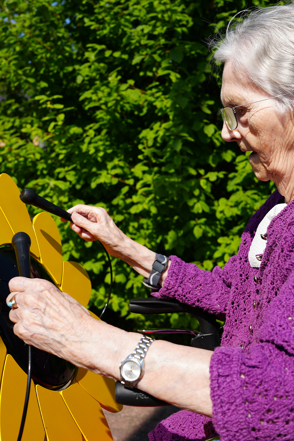 senior lady playing an outdoor drum shaped like a sunflower in a care home garden