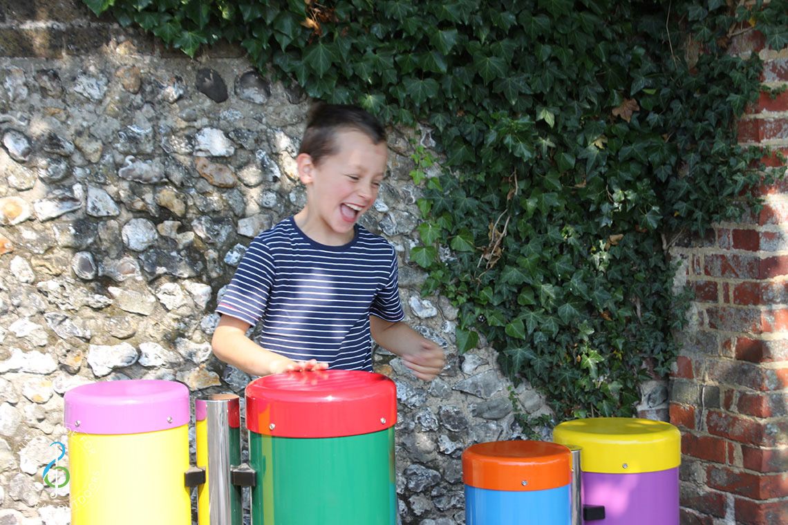 Boy laughing playing on two pairs of colourful outdoor conga drums
