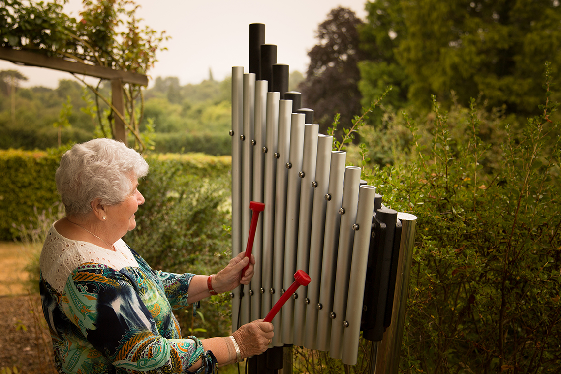 an older lady playing an upright outdoor xylophone in a care home garden