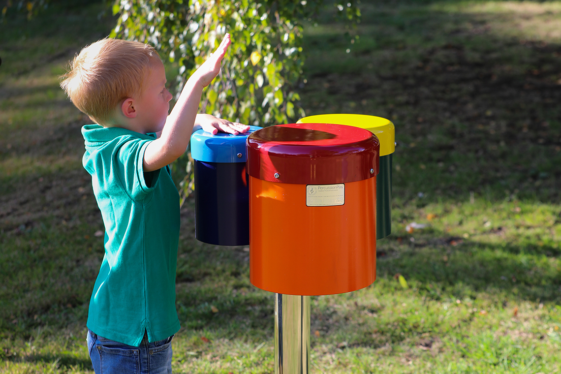 small boy playing rainbow coloured outdoor bongo drums in a school playground