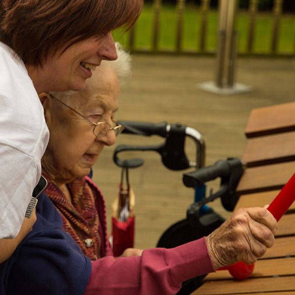 Elderly Lady in Wheelchair Playing a large Outdoor Akadinda xylophone with her carer 