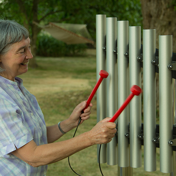 older lady smiling playing a set of outdoor musical chimes 