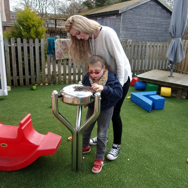 Young girl with special needs and her carer playing a stainless steel tongue drum in school playground