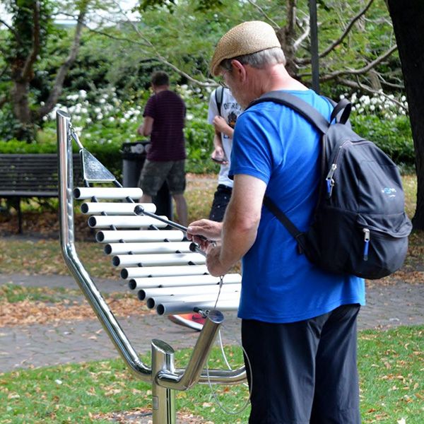 man in a park playing a large metal outdoor xylophone