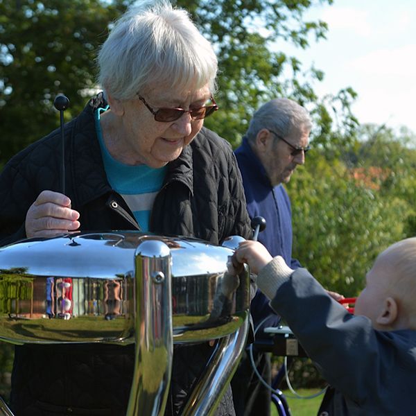 Grandmother and child playing a stainless steel tongue drum in a park