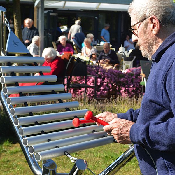 Older man playing an outdoor xylophone in care gome garden