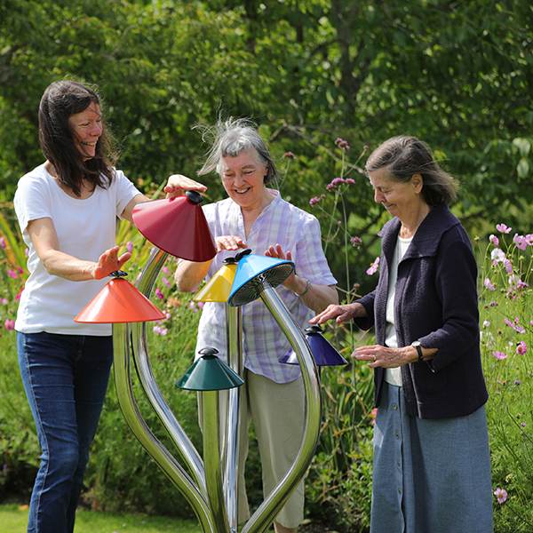 three older ladies playing a large multi-colored outdoor musical instrument resembling Liberty Caps Mushrooms