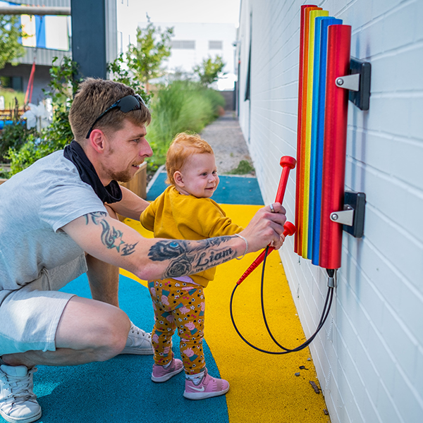 a young red headed girl and her father playing on a set of rainbow colored chimes attached to the wall at the Edinburgh Children's Hospital garden