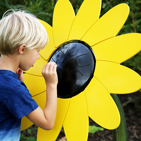 A young boy playing an outdoor musical drum in the shape and colours of a sunflower