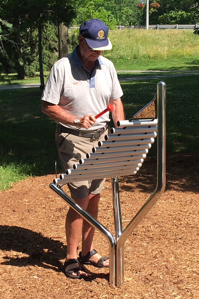 a senior man playing an stainless steel outdoor musical instrument in a rotary music garden
