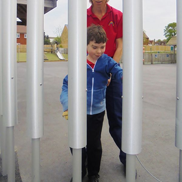 young boy and his carer playing large outdoor tubular bells together in special needs school playground
