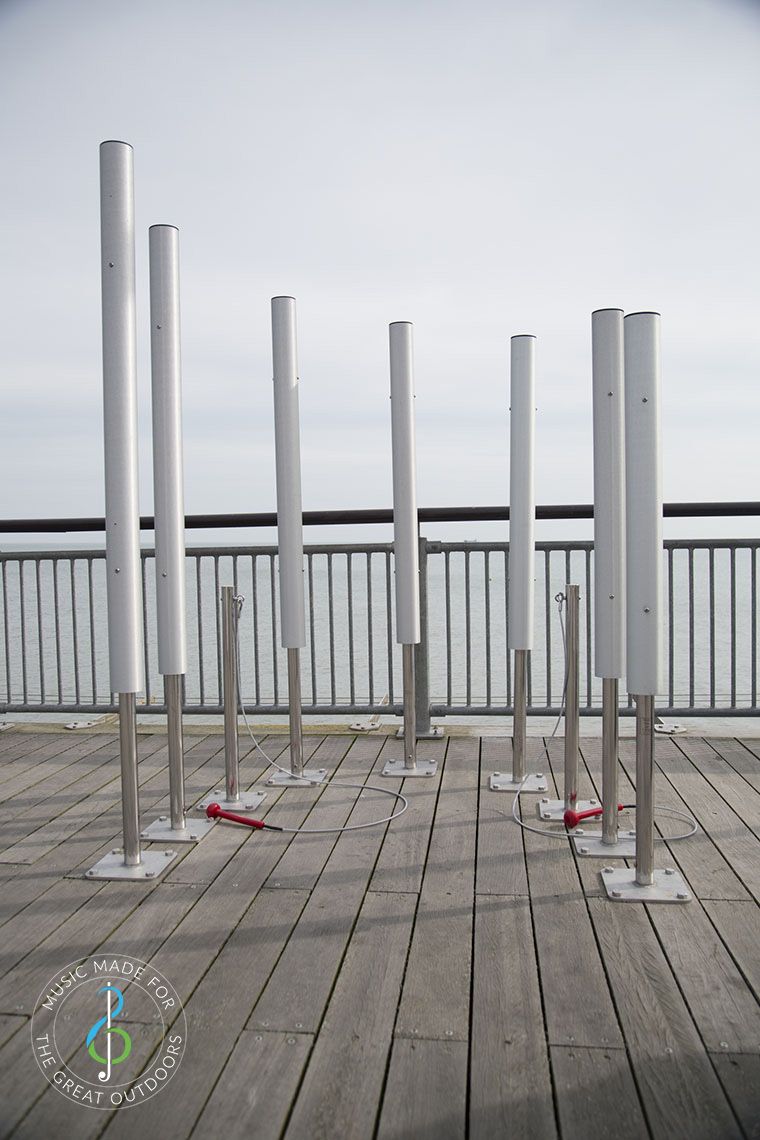 seven tall musical chimes on the end of a pier looking out to sea