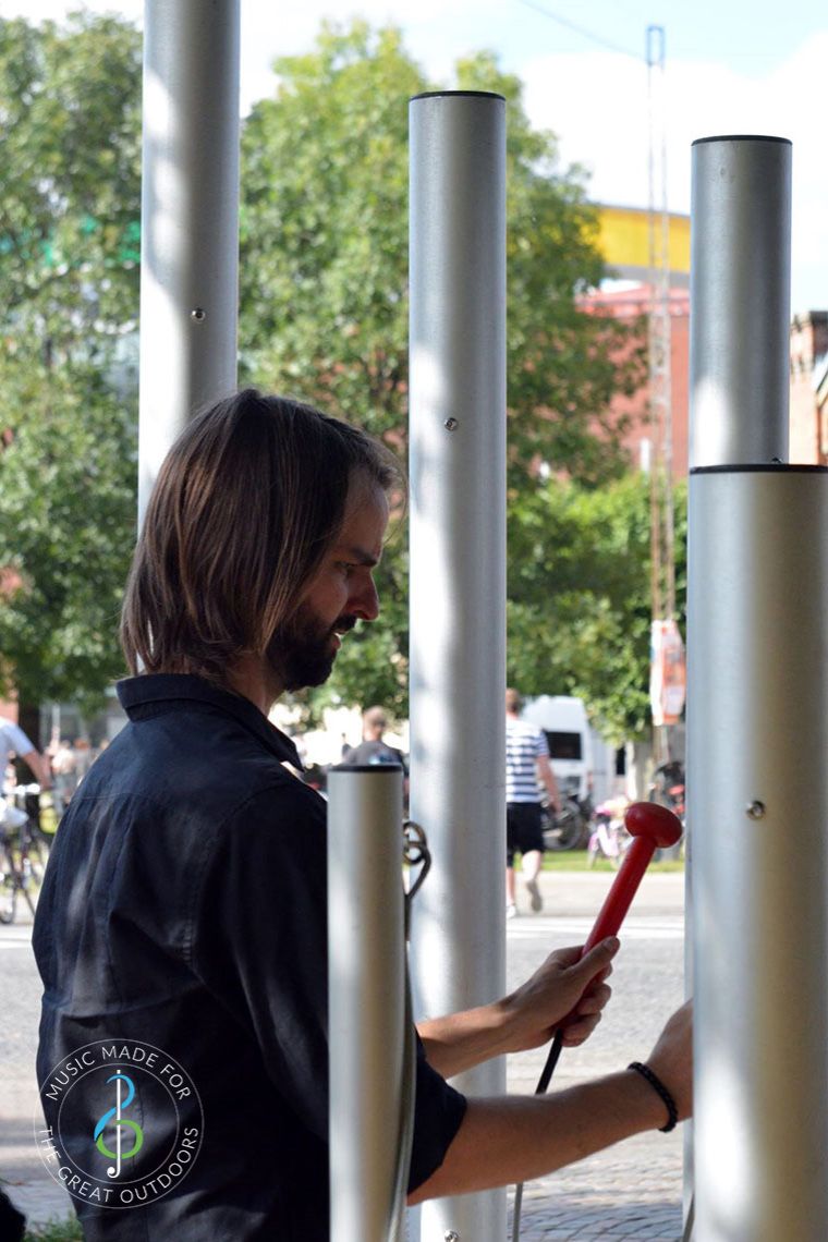 young man hitting large music chimes with a red beater