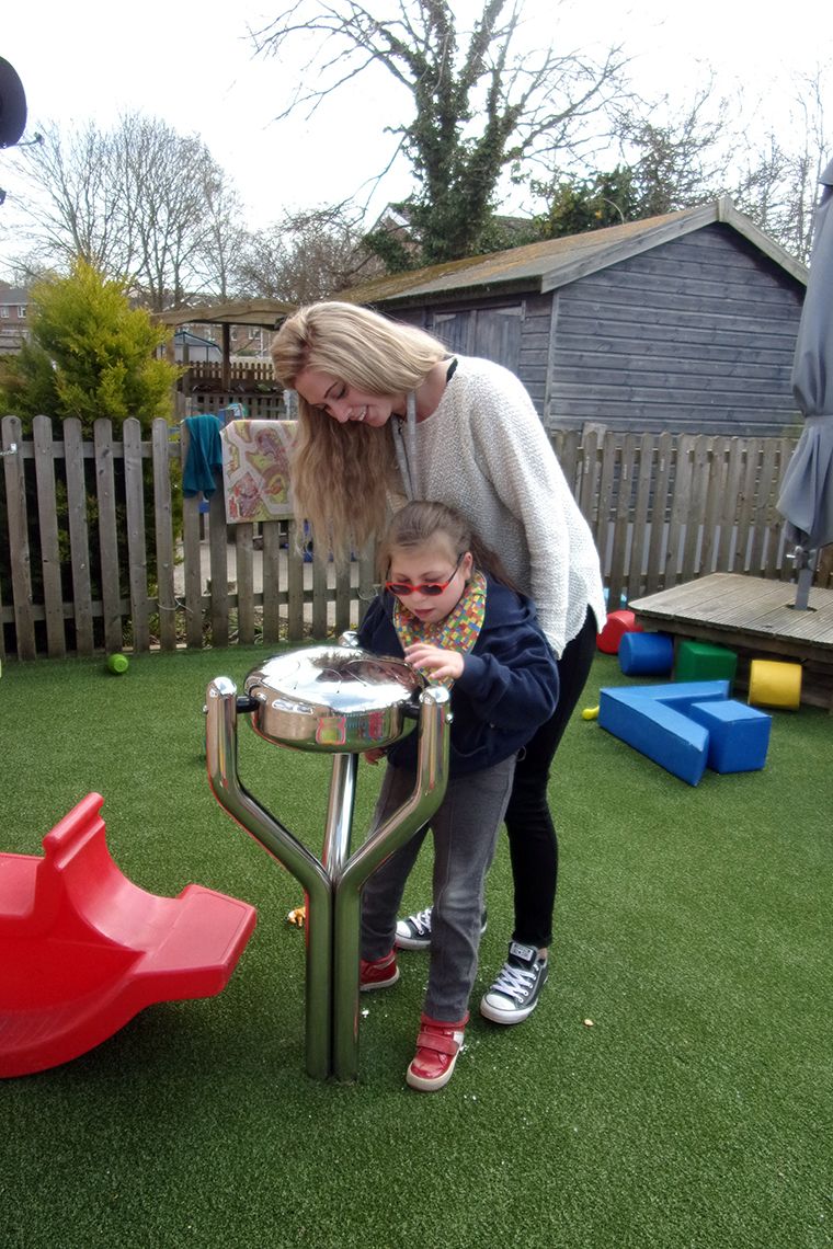 girl with special needs playing a large outdoor tongue drum with her OT