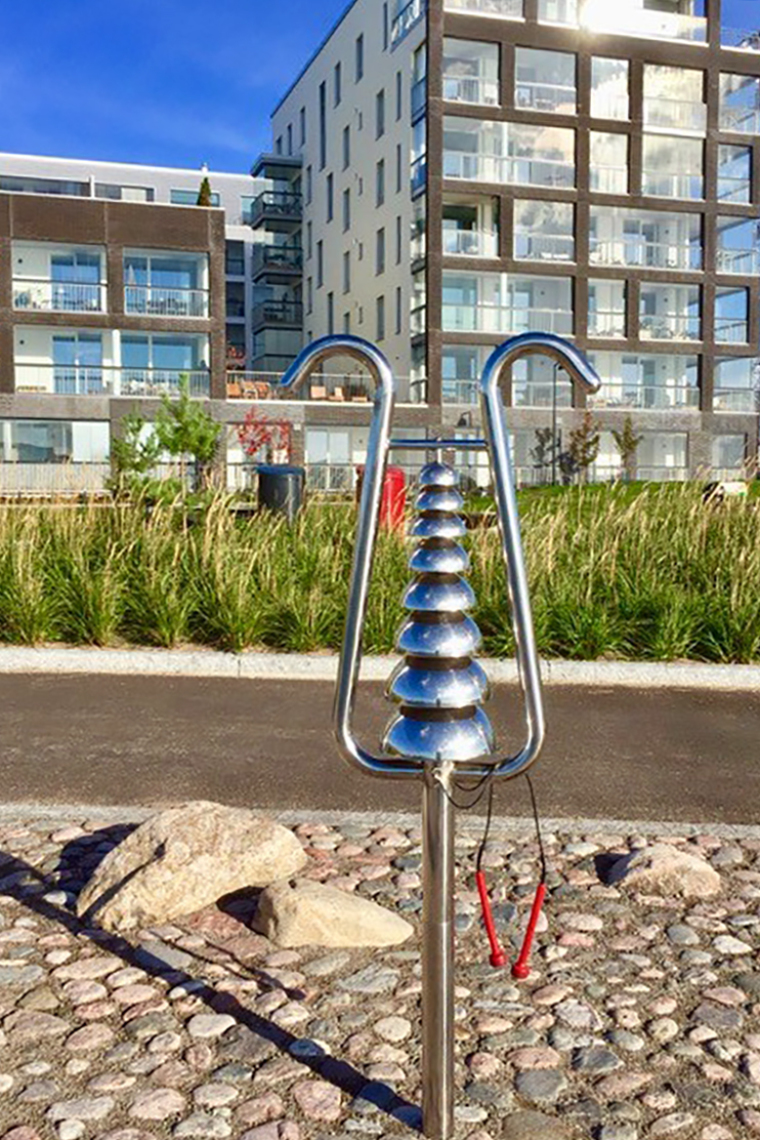 Image of a Percussion Play Bell Lyre - a large outdoor bell tree made of stainless steel - beside an apartment building