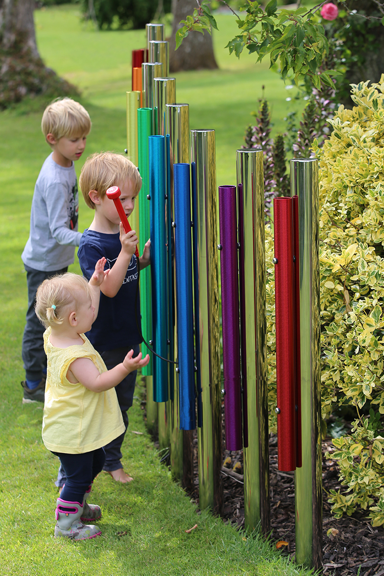 three young children playing on six rainbow colored eco chimes on individual stainless steel posts