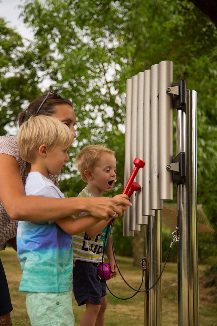 two little boys and their mum playing on an outdoor musical instrument