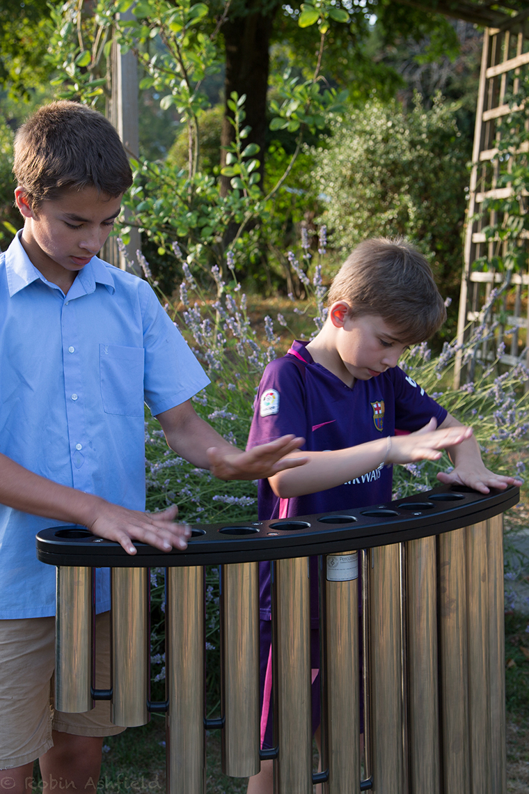 two boys playing a set of handpipes in a park