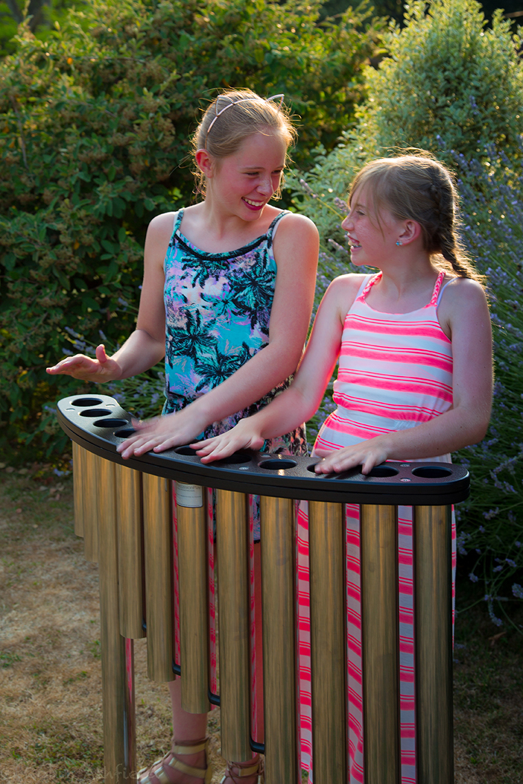 two girls playing a set of handpipes in a park