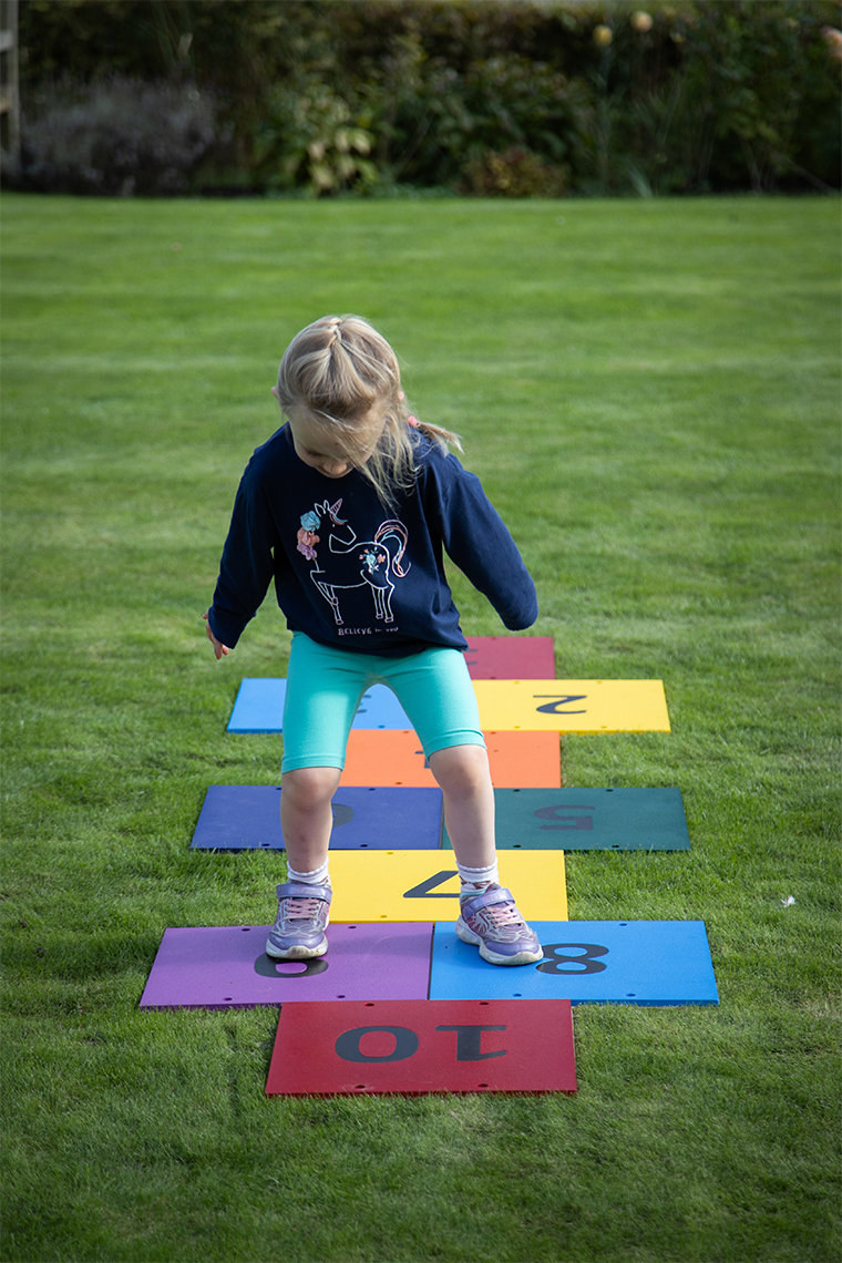 a young girl jumping on an outdoor colourful musical hopscotch installed in grass