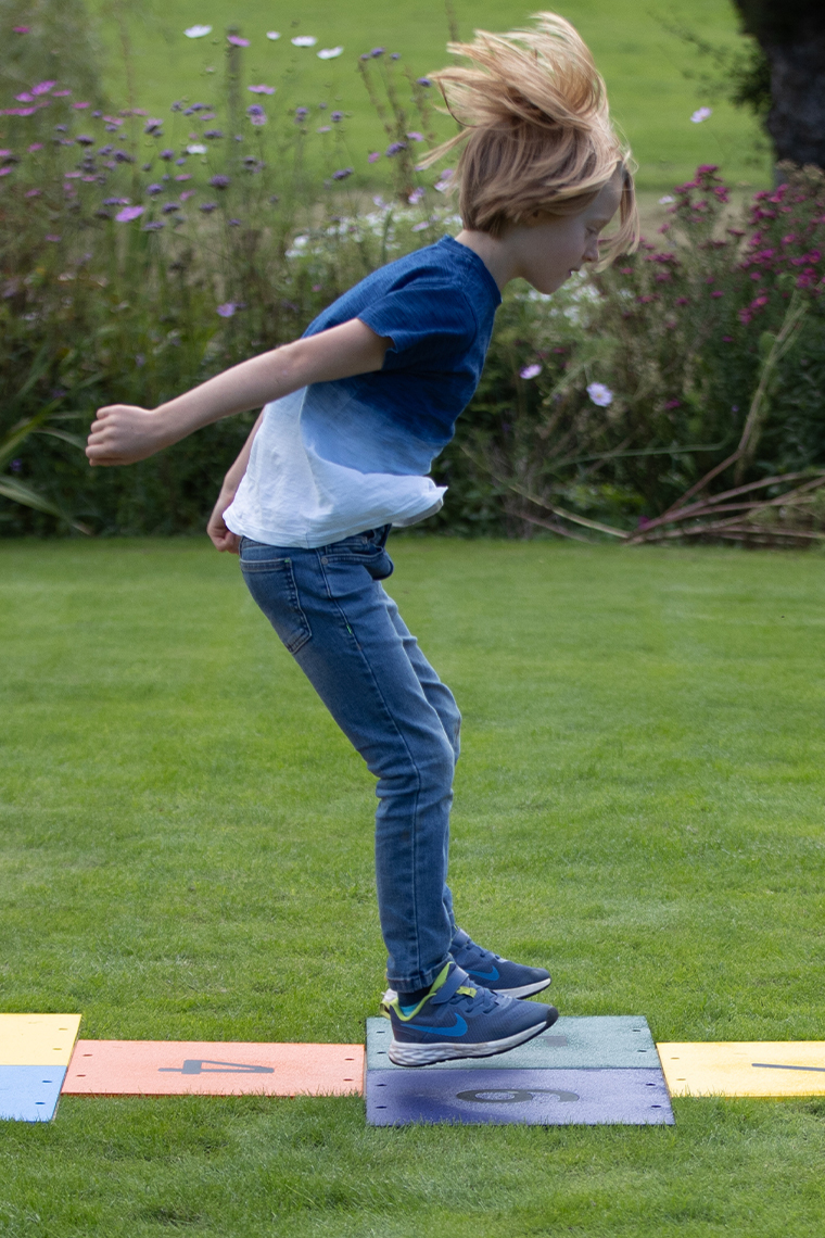 a boy leaping across a colorful outdoor musical hopscotch installed into grass