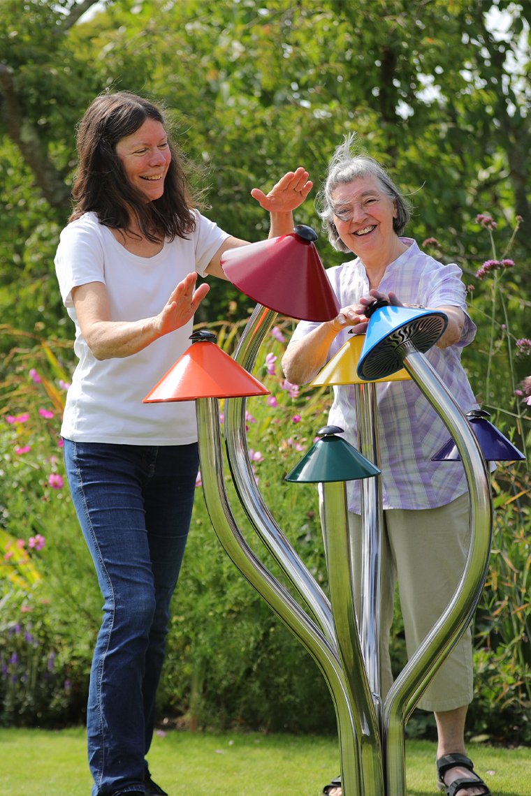 Two older ladies playing a colorful outdoor musical instrument shaped like a cluster of mushrooms in a music park