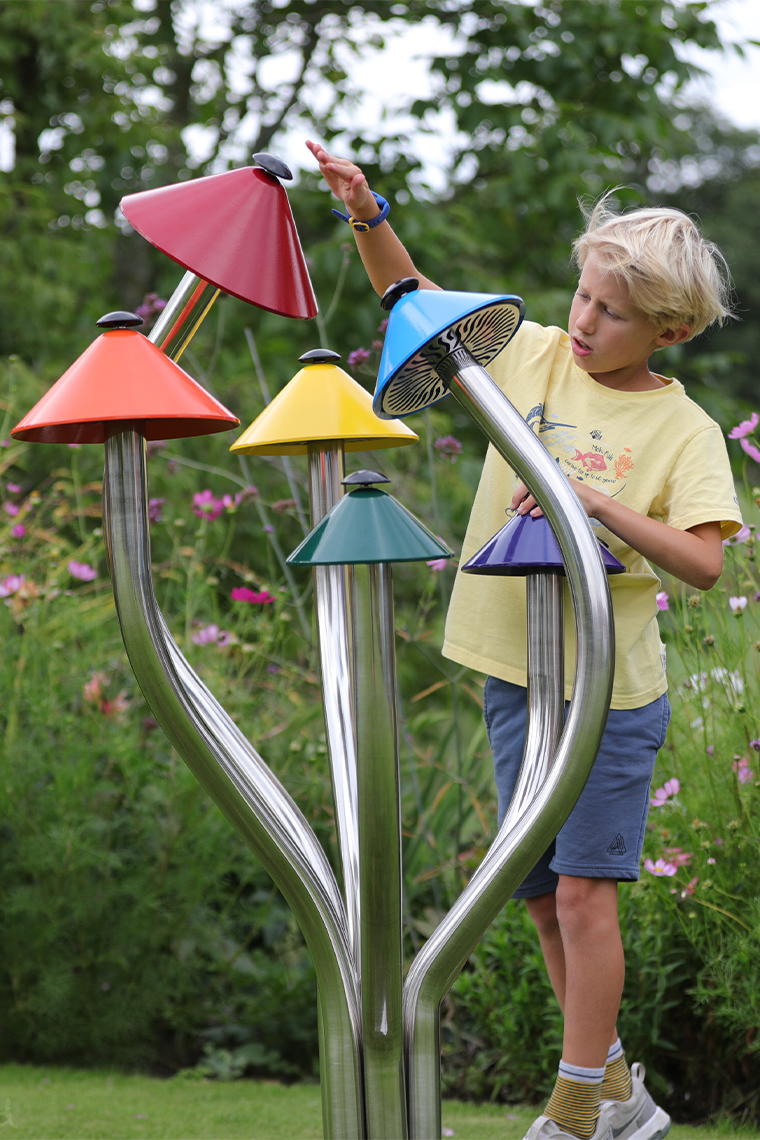 A cluster of musical bells shaped like mushrooms being played in a music park by a young boy