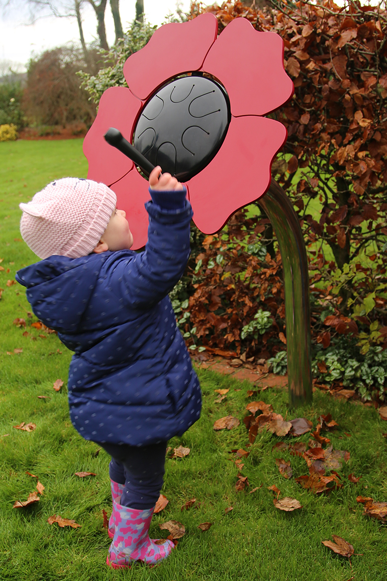 A young boy playing an outdoor musical drum in the shape and colours of a poppy