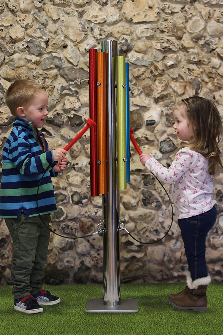 A little boy and girl playing an outdoor musical instrument made of a single stainless steel post and five bright coloured chimes attached