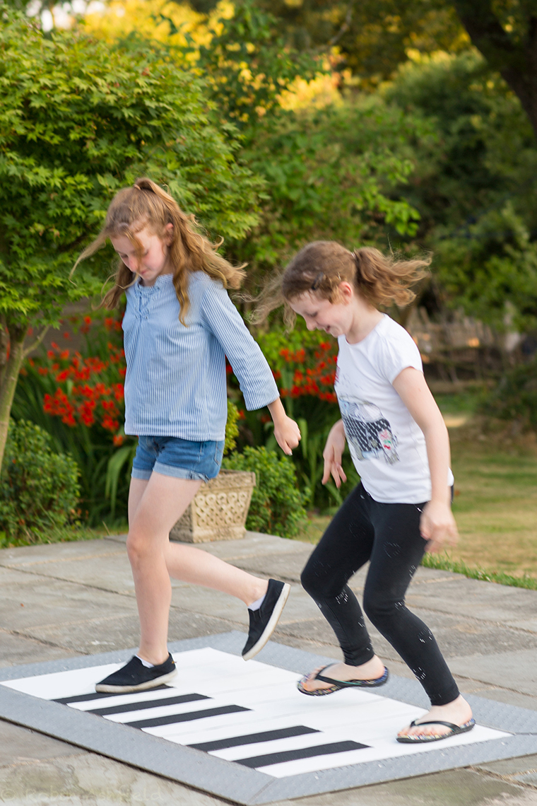 two girls playing on a giant floor piano in a park