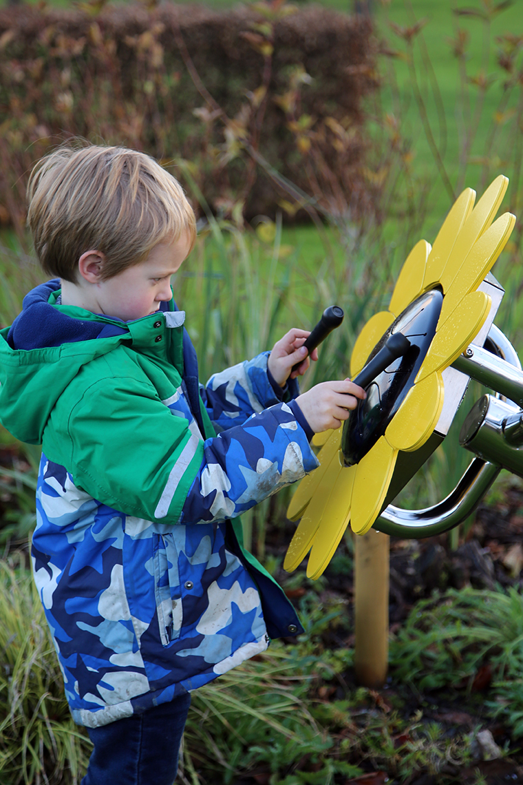 A young boy playing an outdoor musical drum in the shape and colours of a sunflower