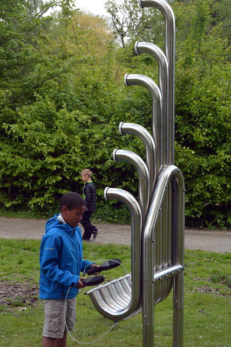 Black boy in a park playing huge silver outdoor musical instrument