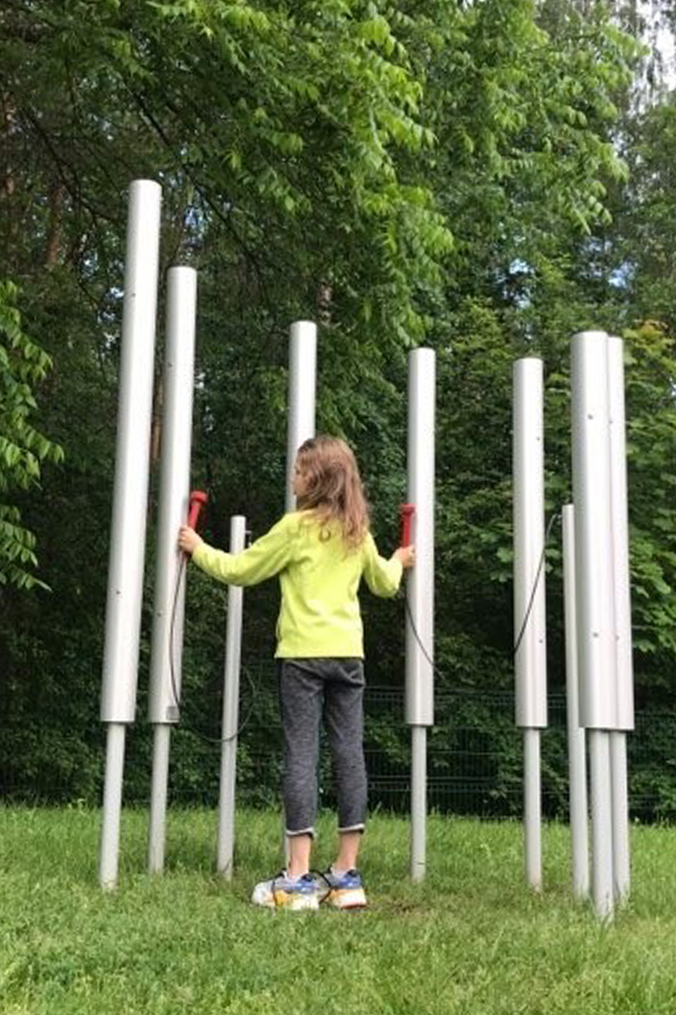 a young girl playing on seven aluminium chimes installed in the ground in a music park
