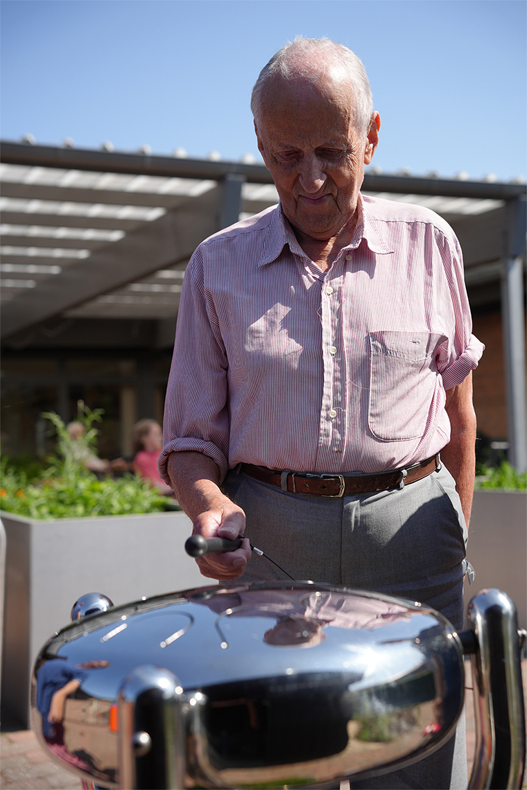 senior man playing a stainless steel tongue drum outdoors in a care home