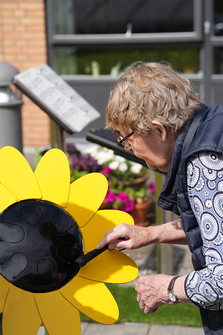 senior lady playing an outdoor drum shaped like a sunflower in a care home garden