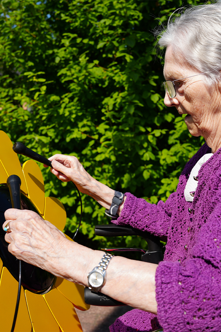 senior lady playing an outdoor drum shaped like a sunflower in a care home garden