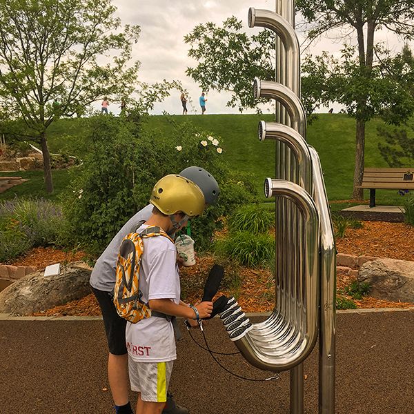 Two skater boys playing a large aerophone musical instrument in a playgroun