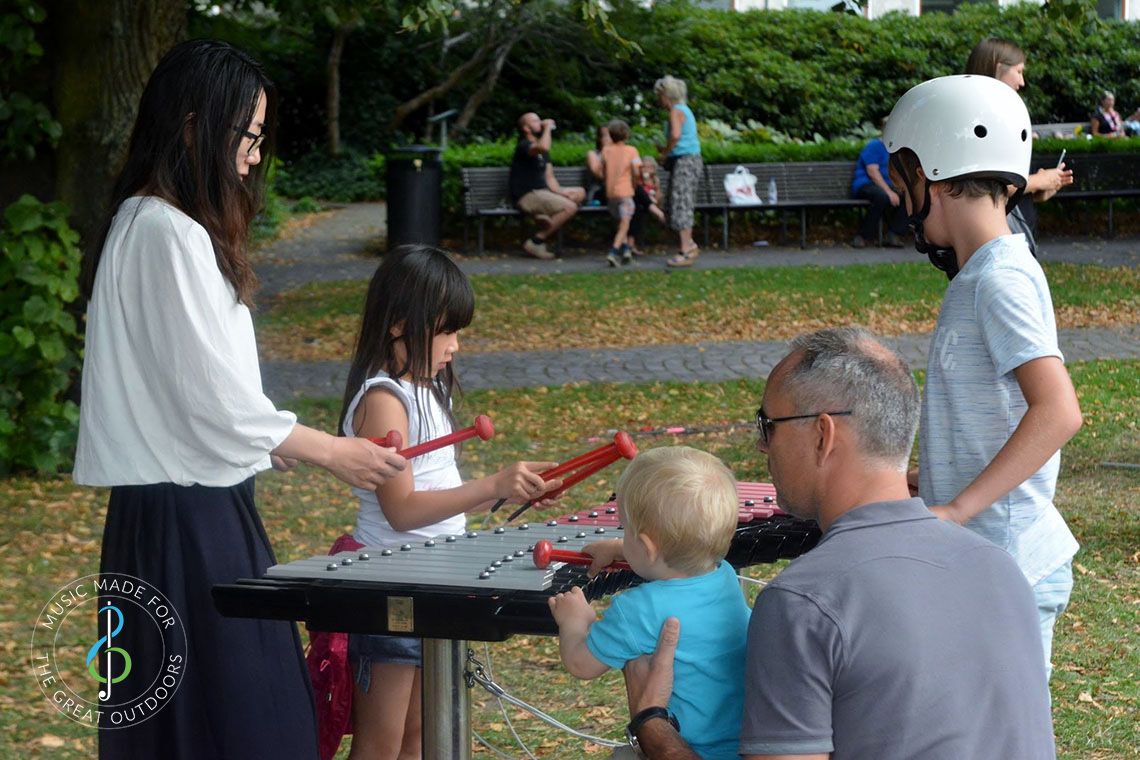 Family playing on large outdoor xylophone together in the park
