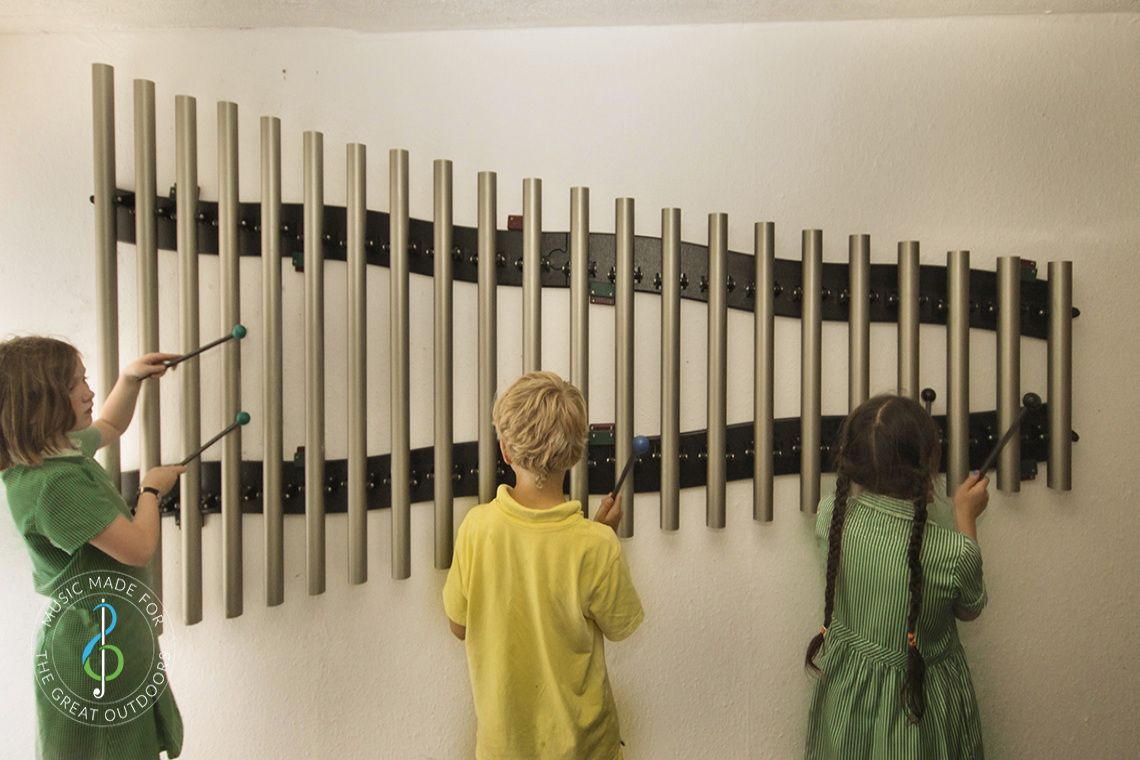three schoolchildren playing on a set of 22 wall mounted chimes