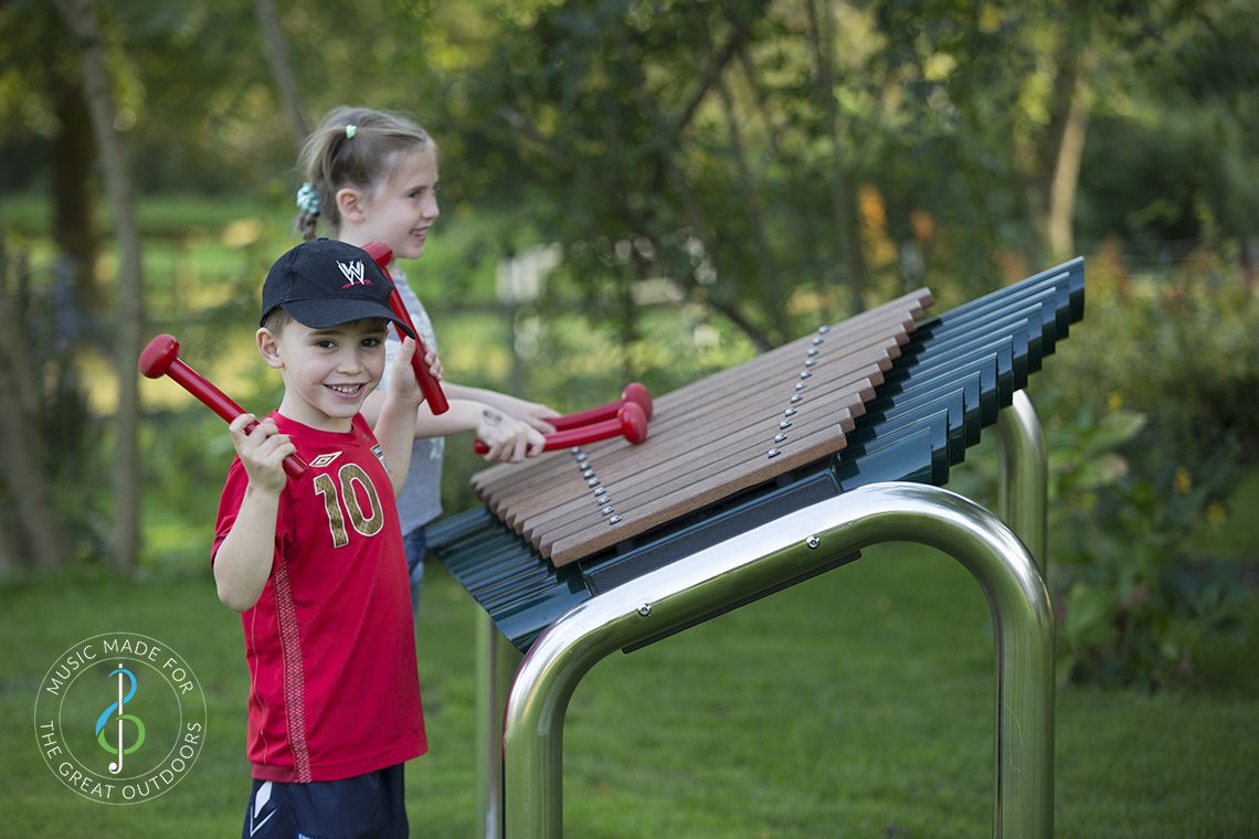 boy smiling and girl inbackground both playing large outdoor marimba xylophone in the park