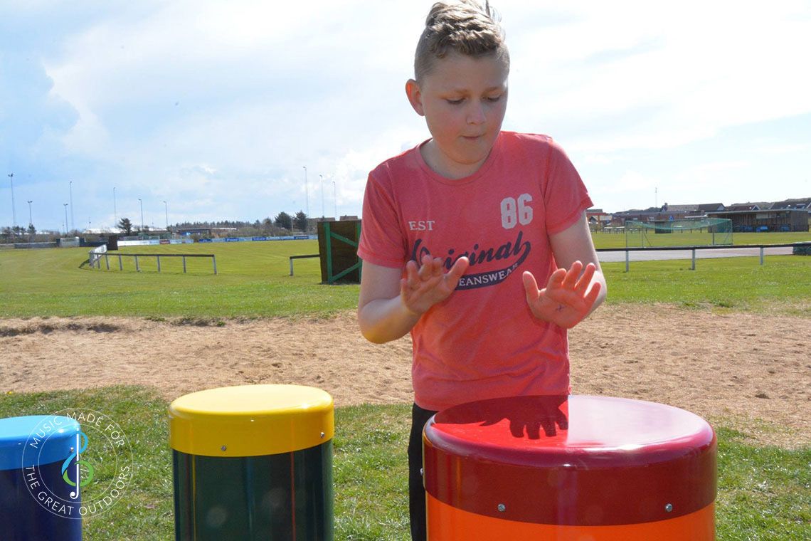 boy splaying outdoor drums with his hands in school playground