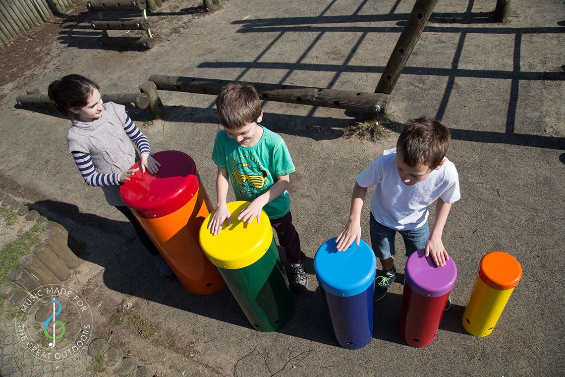 overhead shot of three children playing colourful outdoor drums in a playground